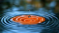 Water drop falling into orange liquid creating concentric ripple circles and splash droplets against dark background, macro photography with selective focus.