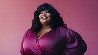 Confident plus size African American woman in purple dress smiling against pink background, showcasing body positivity and modern fashion portrait style.