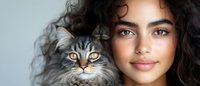 Young woman with curly dark hair holding adorable fluffy kitten with striking yellow eyes. Pet ownership, companionship and bonding concept for lifestyle content.