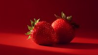 Two fresh ripe strawberries with green leaves on red background creating dramatic lighting and shadows for culinary and food photography projects.
