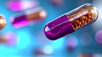 Transparent medical capsule with orange pellets inside on blurred blue background with bokeh effect. Purple and gold pharmaceutical pill macro shot.