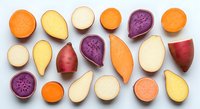 Colorful assortment of fresh root vegetables including sweet potatoes, carrots, beets and parsnips cut in half showing vibrant flesh on white background.