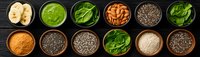 Healthy superfoods collection in bowls on black background including chia seeds, spinach, nuts, banana slices and nutritional powders arranged in row.