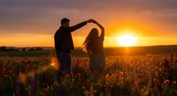 Romantic couple dancing in poppy field at golden sunset creating heart shape with arms, silhouetted against warm orange sky for love and relationship concepts.