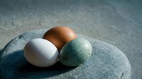 Three natural eggs in different colors resting on smooth stone surface with soft lighting creating peaceful organic composition for kitchen and food concepts.