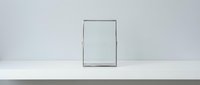 Empty picture frame with thin silver border leaning against white wall on wooden floor in minimalist interior space for mockup and design presentations.
