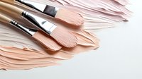 Smooth strokes of nude pink foundation cream smeared on white surface with professional makeup brushes, showing texture and application technique.