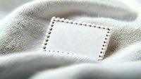 Blank white textile label with stitched border on natural linen fabric background, macro view. Clean empty tag for mockup and branding design.