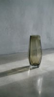 Smoky gray geometric glass vase with faceted design on concrete surface, casting shadows. Modern home decor and interior styling.