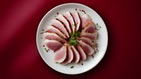 Sliced seared tuna steak arranged in circular pattern on white plate with herb garnish against deep red background. Perfect for food menu or blog.