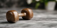 Vintage wooden dumbbell on textured concrete surface with soft natural lighting and shallow depth of field, showcasing minimalist fitness and wellness concept.