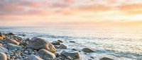 Rocky coastline with golden sunrise light reflecting on calm ocean waters and boulders along the shore, suitable for travel and nature backgrounds.
