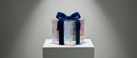Elegant gift box with holographic iridescent wrapping paper and navy blue ribbon bow on white pedestal for luxury present and celebration concepts.