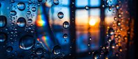 Rain droplets on a window glass with a colorful sunset reflection and rainbow light, creating a moody atmospheric bokeh background.