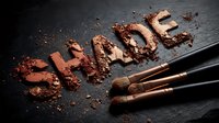 Crushed eyeshadow powder in warm bronze and copper tones arranged with makeup brushes on dark slate surface for cosmetics and beauty design projects.