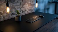 Modern minimalist workspace with wireless keyboard on dark wooden desk, exposed brick wall, pendant lighting and small plant for home office design.