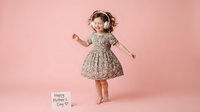 Happy young girl dancing in floral dress on pink background celebrating Mother's Day with joyful expression and playful movement.