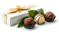 Luxury chocolate truffles with white gift box decorated with golden bow and fresh green leaves on white background, elegant confectionery composition.