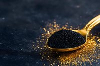 Black caviar on golden spoon against dark background with scattered gold glitter. Luxury gourmet food concept for fine dining and exclusive cuisine.
