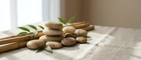 Stacked zen stones with bamboo sticks and green leaves on linen fabric, soft natural light, spa and wellness concept.