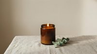 Lit amber glass candle with eucalyptus leaves on marble surface, creating warm ambiance for home decor, wellness, and aromatherapy design projects.