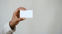 Hand holding blank white business card against neutral background for branding and corporate identity mockup purposes.