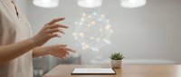 Woman hands presenting holographic network connection icons above tablet on wooden desk with plant in modern office workspace for digital technology concepts.