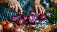 Professional chef slicing fresh red onions on wooden cutting board with coarse salt and herbs, close-up view of culinary preparation in kitchen.