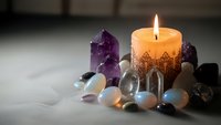 Burning candle with amethyst crystal and healing stones on marble surface for meditation, wellness and spiritual practices.