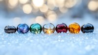 Colorful glass beads arranged in row on sparkling snow surface with soft bokeh background create magical winter atmosphere. Macro photography captures light reflection.