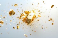 Exploding golden geometric shape with scattered fragments and particles against light background, dynamic motion effect creating dramatic visual impact.