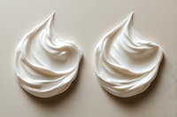 Soft peaks of white whipped cream or meringue swirls on beige background, showing light and shadow detail in minimalist food photography composition.