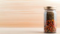 Glass jar filled with layered colorful peppercorns on wooden background, black and red spices for cooking and seasoning in minimalist composition.
