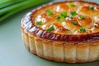 Fresh baked quiche with flaky pastry crust, creamy egg filling and chopped green onions garnish on light background, close up view of homemade savory pie.