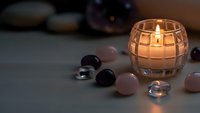 Glowing candle in glass holder surrounded by healing crystals and gemstones creating peaceful meditation atmosphere for wellness and spiritual practices.