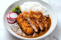 Crispy breaded pork cutlet served with steamed white rice, fresh radish slices and curry sauce on white ceramic plate against marble background.