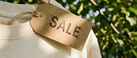 Kraft paper sale tag hanging on white clothing with green nature background, retail discount concept for fashion and shopping promotions.