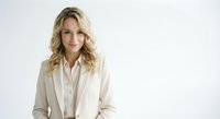 Professional blonde businesswoman in beige suit smiling confidently against white background for corporate marketing and business presentations.