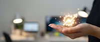 Person holding glowing light bulb with sparks in office environment, representing innovation, ideas, energy efficiency, and creative business solutions.