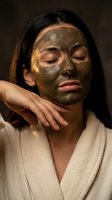 Young Asian woman enjoying luxurious gold clay face mask treatment in spa bathrobe for skincare and wellness routine.