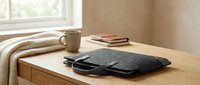 Cozy workspace setup with laptop bag, coffee mug and books on wooden desk near window. Warm natural lighting creates productive home office atmosphere.