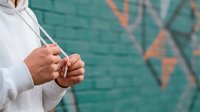 Young adult male professional in white shirt holding tablet device against urban teal brick wall with orange geometric graffiti art, suitable for business technology and corporate concepts.