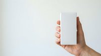Person with medium skin tone holding blank white rectangular box or packaging against neutral background, suitable for product mockup, branding, and marketing materials.