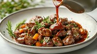 Tender beef meatballs in rich tomato sauce with fresh herbs being poured from ladle onto white plate for gourmet dining experience.