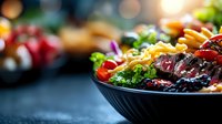 Fresh mixed salad with grilled beef strips, cherry tomatoes and pasta in black bowl on dark background with bokeh lights, macro food photography.