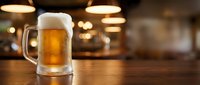 Fresh golden beer with white foam head in glass mug on wooden bar counter in cozy pub atmosphere with warm lighting for hospitality and beverage concepts.