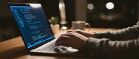 Software developer coding on laptop in cozy workspace with coffee cup, programming late night session for web development projects.