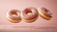 Pink glazed donuts with colorful sprinkles floating in air against soft pink background, creating magical levitation effect for bakery and confectionery marketing.