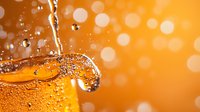 Refreshing golden liquid with bubbles and droplets splashing against vibrant orange bokeh background, macro photography capturing dynamic beverage motion.