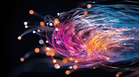 Glowing fiber optic strands in pink, blue and orange colors creating dynamic light trails against dark background with bokeh effect and motion blur.